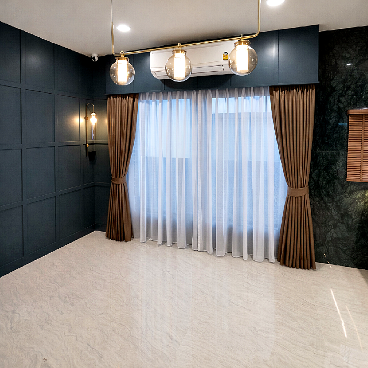 ห้องโมเดิร์นที่มีผ้าม่านจีบน้ำตาลผูกเปิดคู่กับม่านโปร่งสีขาว หน้าต่างบานใหญ่ ผนังสีน้ำเงินและหินอ่อนดำ พร้อมโคมไฟแขวนสามดวง